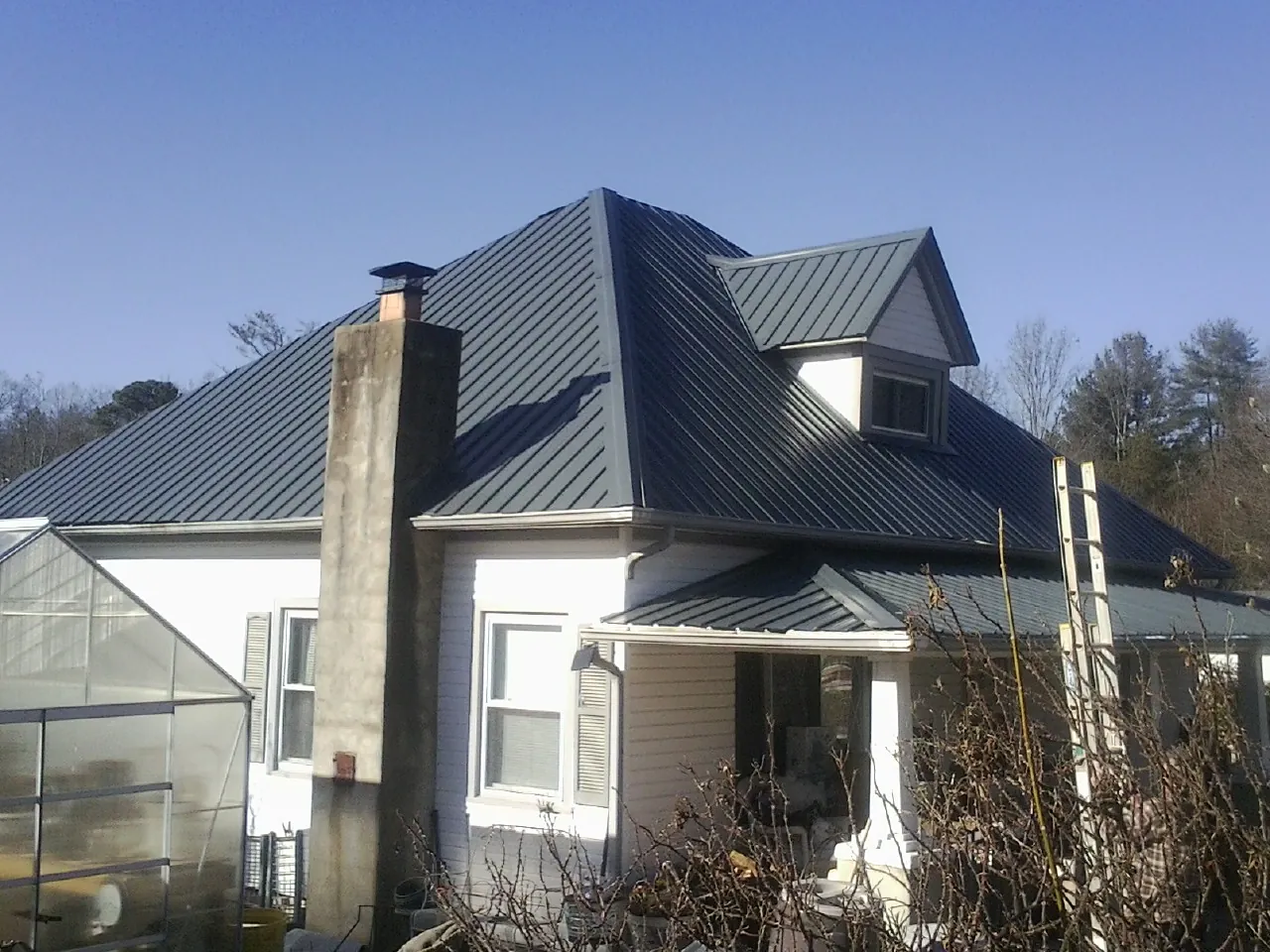 Dark blue standing seam metal roof on a white farmhouse with dormer — Slate & Tile Roof Repair by Roofing Brothers in Humansville
