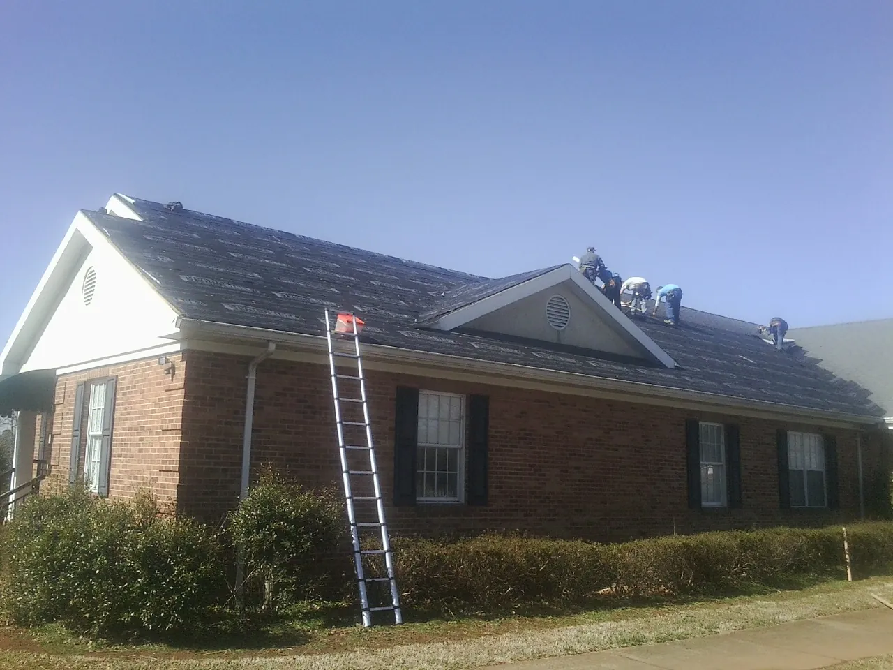 Crew tearing shingles off a brick ranch roof with a ladder set — Emergency Roof Repair work by our crew in Humansville