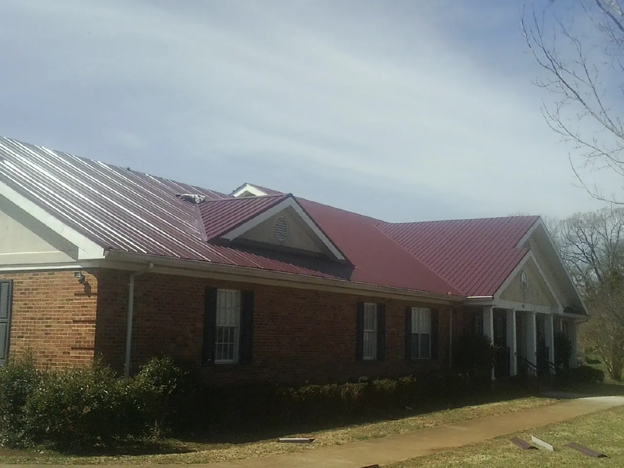Red metal roof with gabled entries on a long brick building, from a Hail Damage Roof Repair job in Humansville