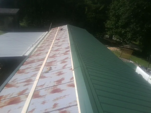 Old rusted panels beside newly installed green metal roofing — Wind Damage Roof Repair by Roofing Brothers in Humansville