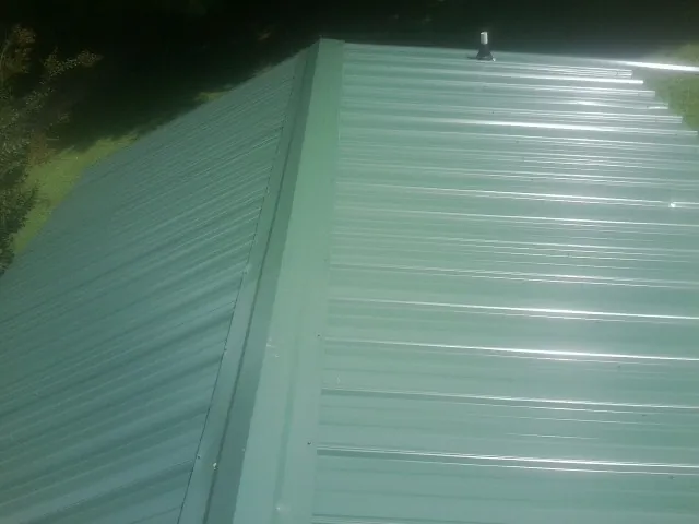 New green metal panels meeting at the ridge of a roof — Flat Roof Repair work by our crew in Humansville