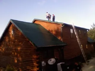 Crew on the ridge of a green metal roof on a two story log home in Humansville