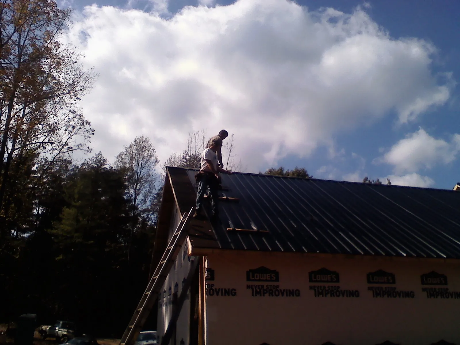 Roofer fastening dark metal panels high against a cloudy sky, from a Roof Inspection job in Humansville
