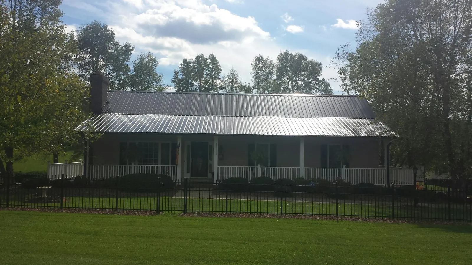 Gray metal roof on a brick ranch with a full width front porch — Gutter Guard Installation work by our crew in Humansville