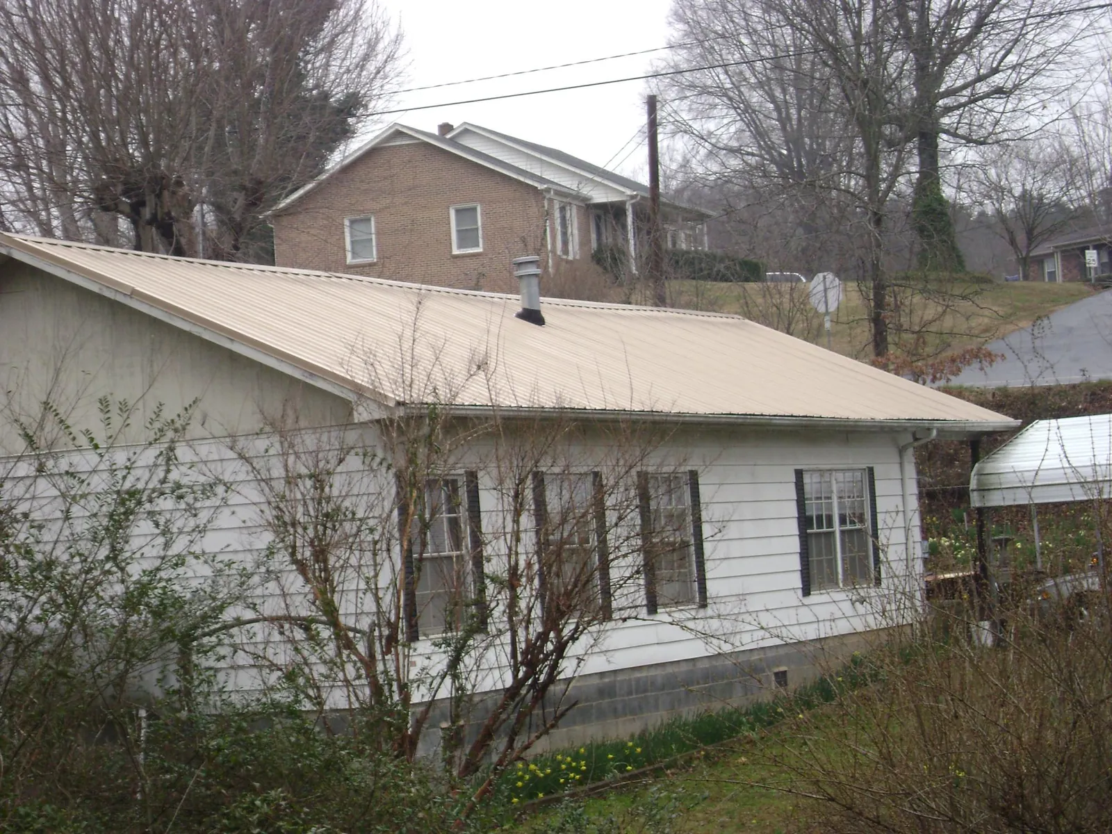 Tan metal roof on a white sided house set into a hillside — Commercial Roofing by Roofing Brothers in Humansville