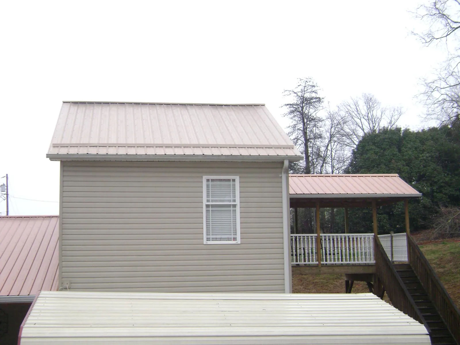 Tan metal roofs on a two story addition and attached porch, from a Roof Replacement job in Humansville